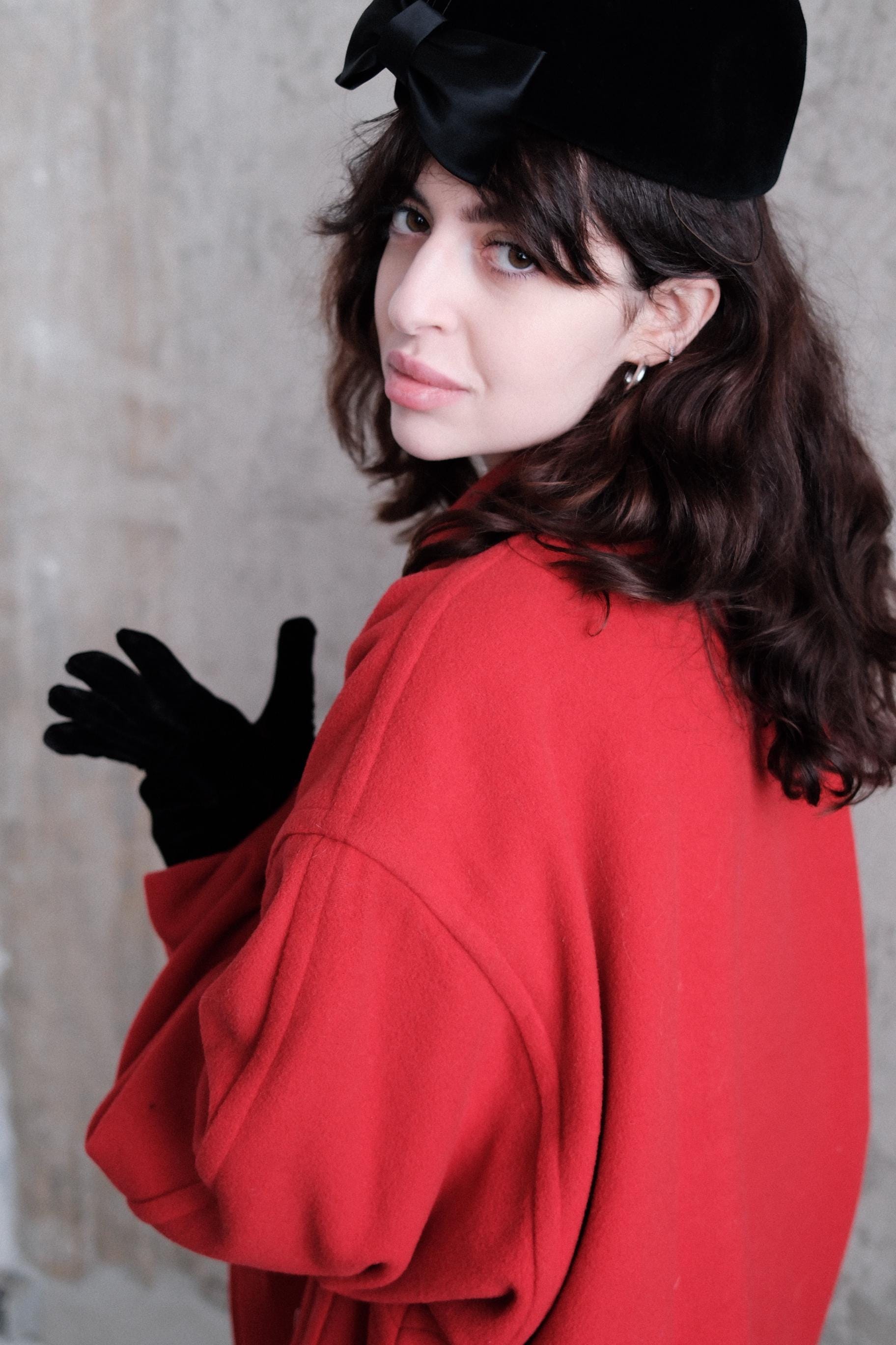 A woman wearing a red coat and black gloves is lying on her stomach, with her head tilted back and her eyes looking up.