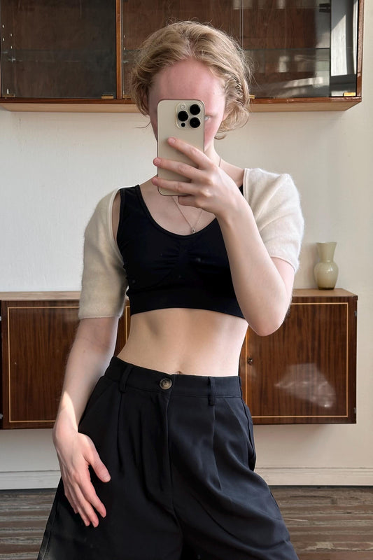 A woman is taking a selfie with her phone, holding it up to her face, and wearing a black top and black pants.